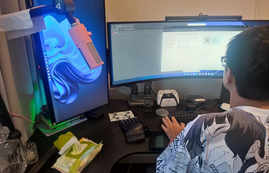 Người dùng ngồi trước màn hình cong siêu rộng và một màn hình dựng dọc nền Windows 11.