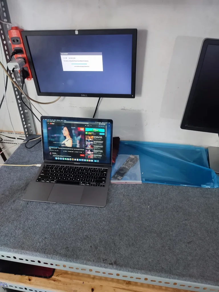 MacBook Air chạy thử trên bàn sửa chữa, phía sau màn hình Dell báo không có tín hiệu VGA