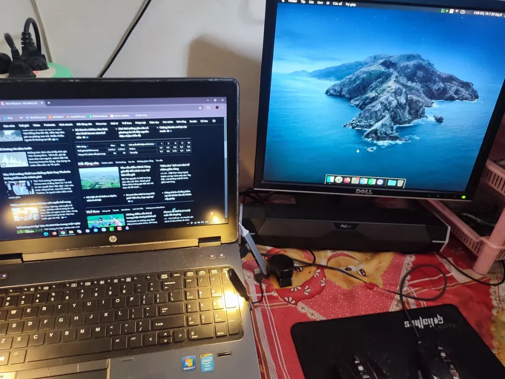 Laptop HP mở nắp đặt cạnh một màn hình rời Dell đang hiển thị giao diện macOS trên bàn làm việc.